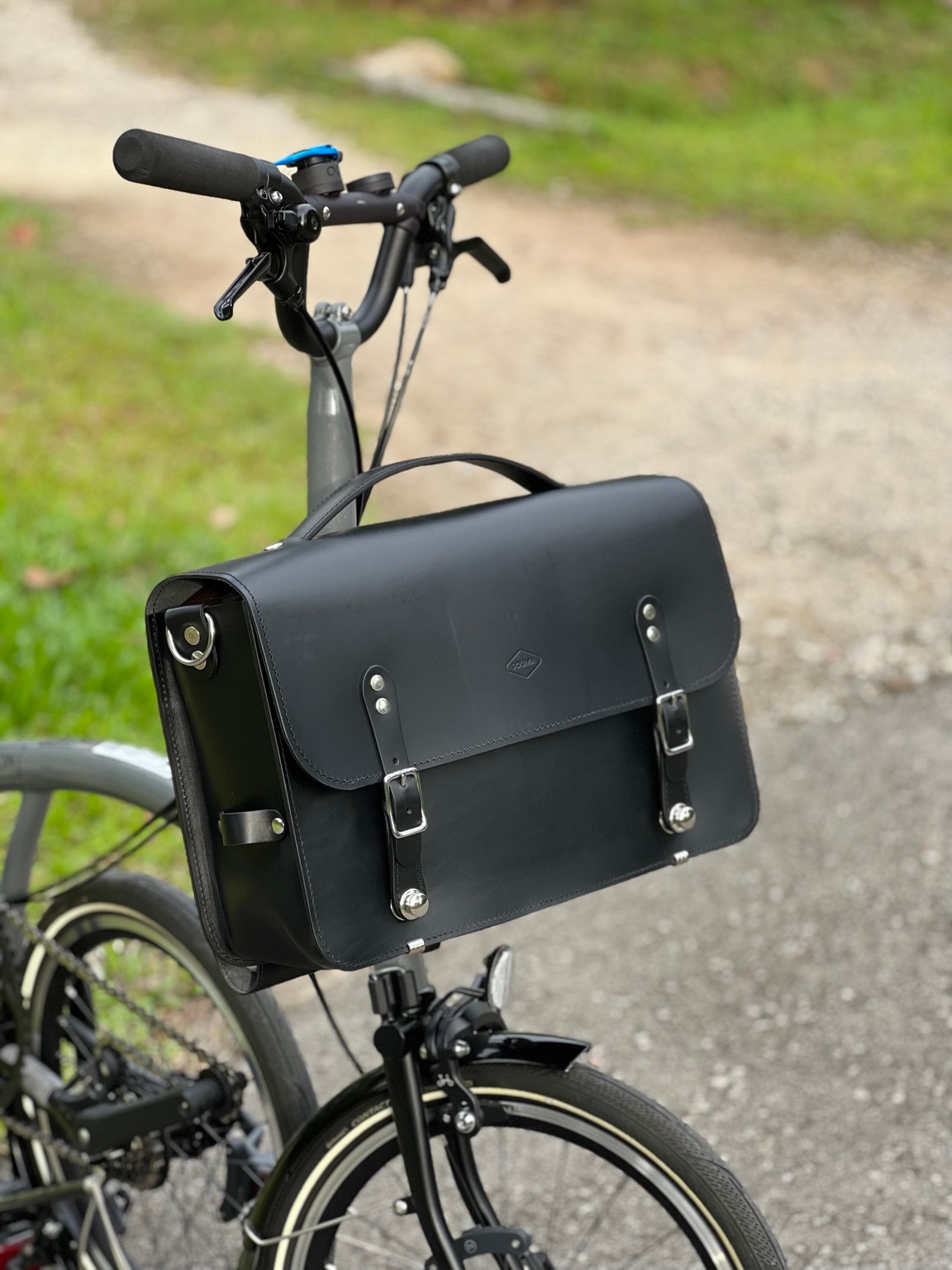 Black Souma Leather camera bag on a Brompton, three-quarter view