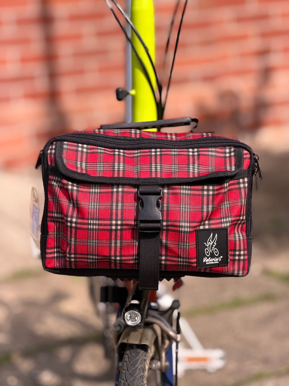 Front view of Valeria’s Cris Mini #04 red tartan Brompton bag with black buckle, trim and sewn brand label